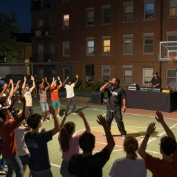 an old school hip hop concert taking place on a basketball court behind a large brick apartment at night, many people dancing with their hands in the air, a rapper is standing on stage yelling into the mic, a dj with audio equipment at the back of the stage, in the style of frank frazetta