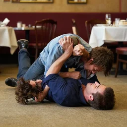andy richter in a restaurant laying belly first on the floor being put into a sharpshooter wrestling move