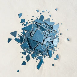 aerial photography high contrast angular sharp cool blue slate shards scattered loosely chaotically in the pale sand
