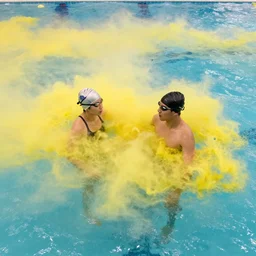 two people in a swimming pool with cloud of yellow water surrounding them