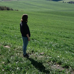 woman on hill overlooking field, drenched in shadow, green fields, in profile