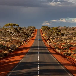 a long road in the red australian outback, a lone blue car is seen in the distance