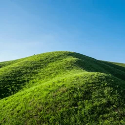 a singular, green hill in the middle of the photo. no tree's are on the hill. the sky is a bright blue.