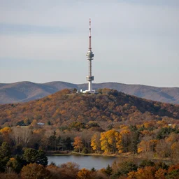 a hill with a radio tower next to a pond, autumn hills in background. telephoto lens photography.