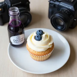 dslr food photograph of a blueberry cupcake white creme topping and a bottle of blueberry sauce on the side, aerial view, narrow shot, hasselblad, 1 0 0 mm f 1. 8