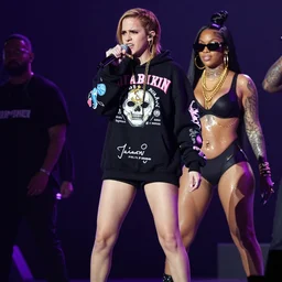 angry full body Emma Watson singing on rap concert stage with mic wearing designer hoodie as doja cat as cardi b wearing gold chain and sunglasses and gold hoop earrings