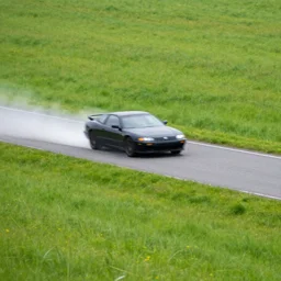 a speeding car on a small grey road in a grassy field