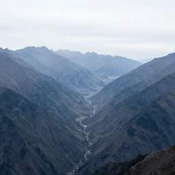 Panoramic photo where the mountains are towering over the valley below their peaks shrouded in mist. The sun is just peeking over the horizon and the sky is ablaze with colors. The river is winding its way through the valley and the trees are starting to turn yellow and red