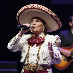 an old lady rapping on stage. The old lady is wearing a sombrero and a thick gold chain. Professional live venue photography.