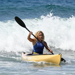 Trixie Mattel paddling in a canoe in the ocean with huge waves