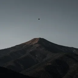 a black dot in the sky stretching out a mountain, dark lighting, landscape