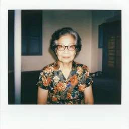 polaroid photo of an old chinese singaporean woman with permed hair, glasses, wearing a floral dress