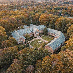 low drone shot of a Disney style ranch style School campus in the middle of the Woods during autumn