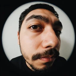 fish eye lens close up photograph of a man with a goatee side eyeing the camera with a sympathetic look