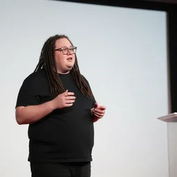 an obese white skinned entrepreneur with long black dreadlocks and trendy glasses gives a ted talk inside a large aquarium of neon jellyfish, high detail, sharp focus, depth of field, hyper realistic, time magazine 2 0 2 2