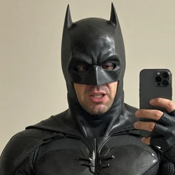 bruce wayne with a honest reaction, taking a selfie, grainy quality, low quality, low resolution, realistic, hyperrealistic, very realistic, hd quality, intricate details, very detailed, grainy, taken on an iphone, awkward angle, awkward lighting