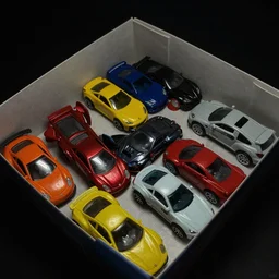 a badly lit photo taken by an old phone of a box full of toy cars.