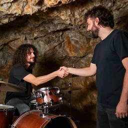 jd beck shaking hands with a curly haired drummer in a cave