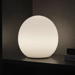 a lamp sitting on a shelf in a dark room. the lamp is shaped like totoro. the room is dark. the lamp lights the room. comic books on shelf behind lamp
