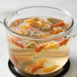a clear glass pot filled with boiling water and rainbow colored pasta