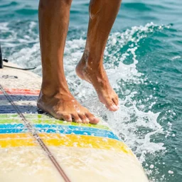 Toes of a surfer hanging ten on the edge of a colorful striped surfboard with turquoise waves , cinematic, hyper realism, high detail, octane render, 8k“