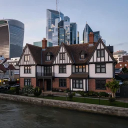 realistic photo of a tudor style detached house surrounded by skyscrapers, a river flowing through the scene, dusk