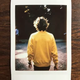 instax polaroid film photo of a young man with messy medium length light brown hair and a yellow sweater walking away from the camera with a nailbat, zoomed out, warm, nostalgia, faded glow, expired film analog photography, grainy texturized dusty, saturated colorized