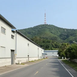 a road next to warehouses, and a hill background with a radio tower on top