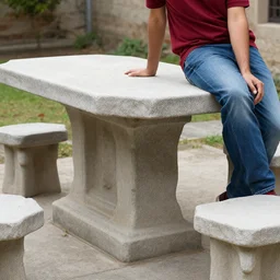 table made of stone with man leaning on it wearing jeans and a red shirt