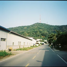 a road next to warehouses, and a hill behind it with a radio tower on top, disposable camera effect