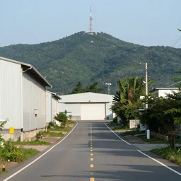 a centered road next to warehouses, and a hill background with a radio tower on top, 3 0 0 mm telephoto lens