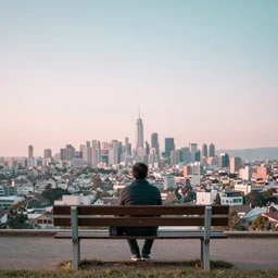 a long exposure photograph of a man sitting on a bench overlooking a cityscape. Wide angle, pastel colours