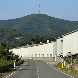 a road next to warehouses, and a hill background with a radio tower on top, 3 0 0 mm telephoto lens